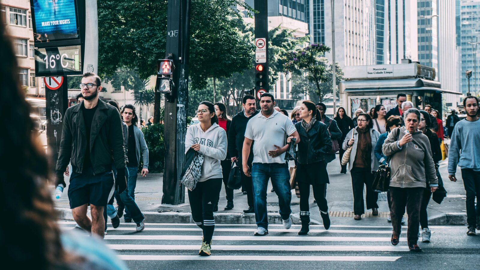 A diverse group of people crossing a street in a bustling city setting with skyscrapers.