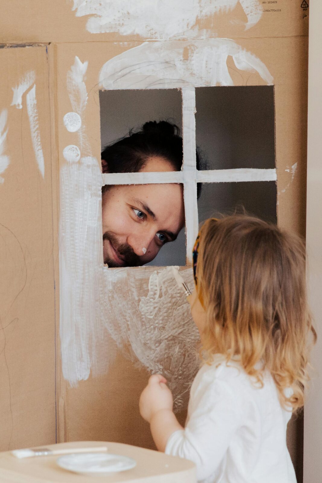 Father and child enjoy creative play with a cardboard house indoors.